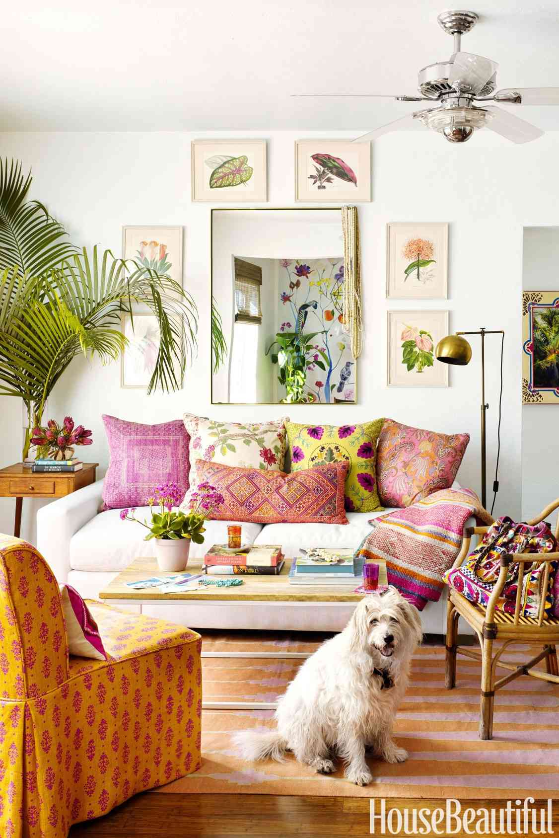 Samperton's living room with botanical artwork, patterned cushions, and a movable coffee table; photograph credited to Annie Schlechter in House Beautiful.