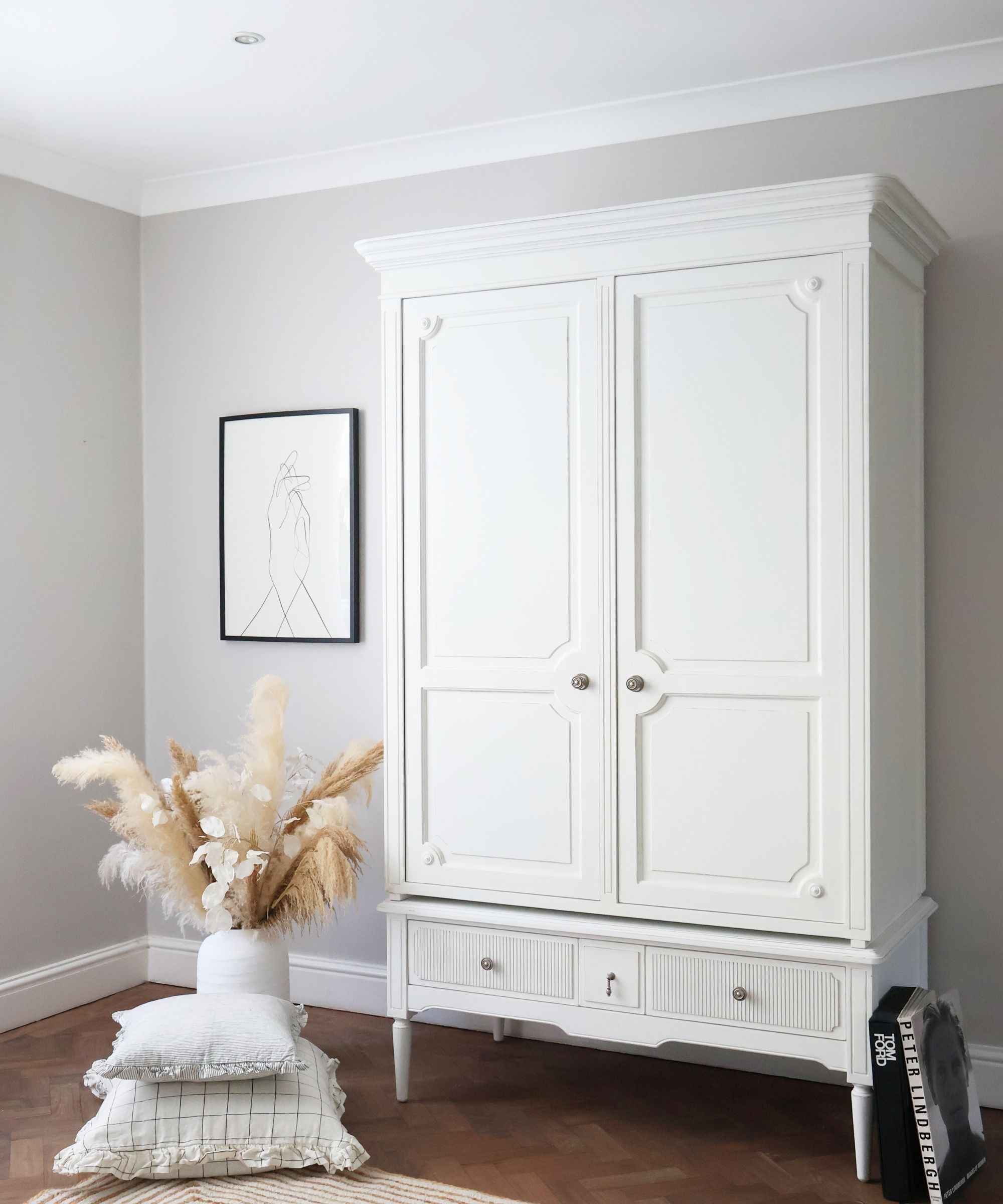 The reference illustrates a contained bedroom storage area with a freestanding white wardrobe rather than belongings left across the floor.