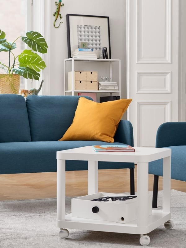 The source wheeled side table sits beside a sofa with objects on its top and lower shelf, illustrating a movable supporting surface.