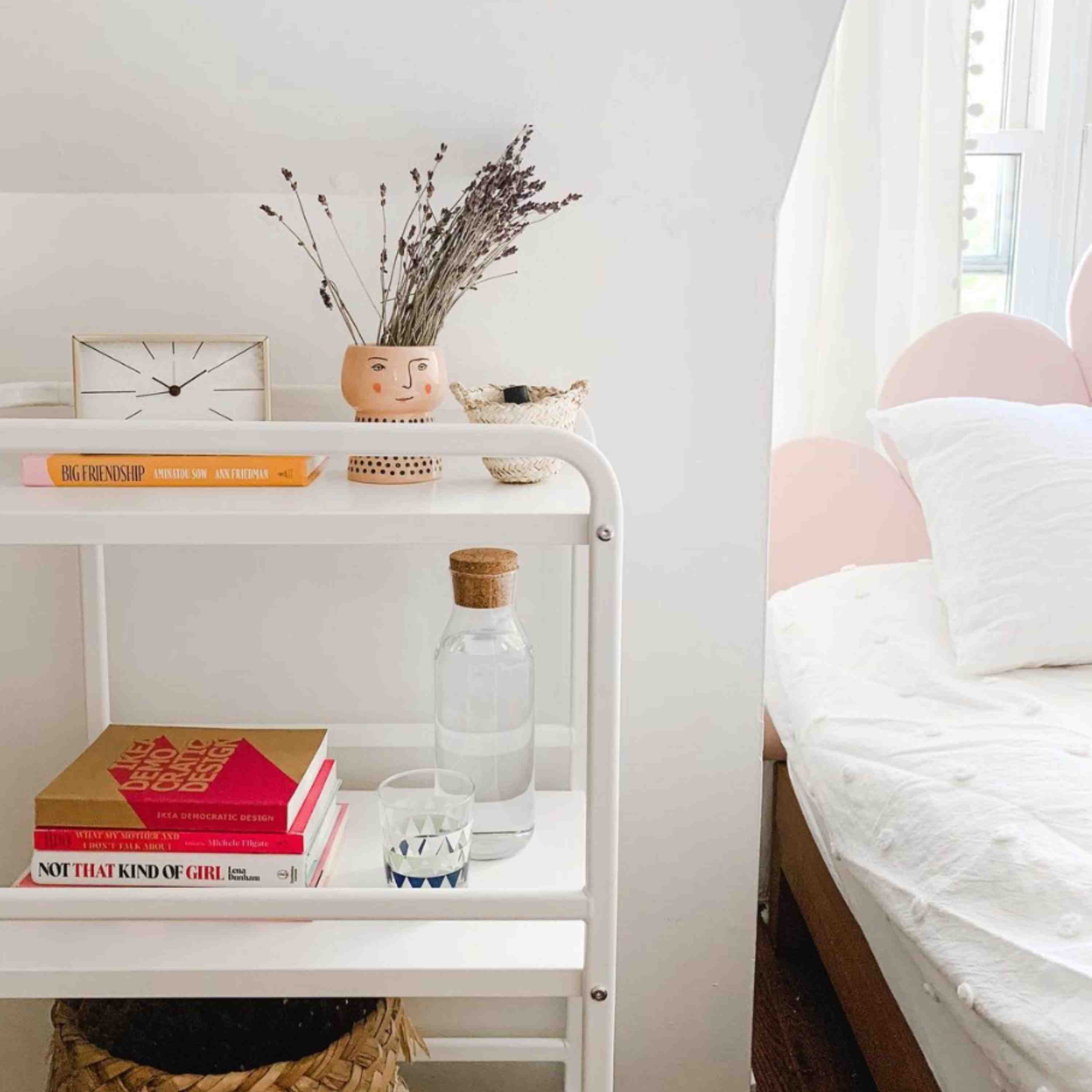 The reference uses a white bar cart as a bedside surface for books, water, and smaller essentials.