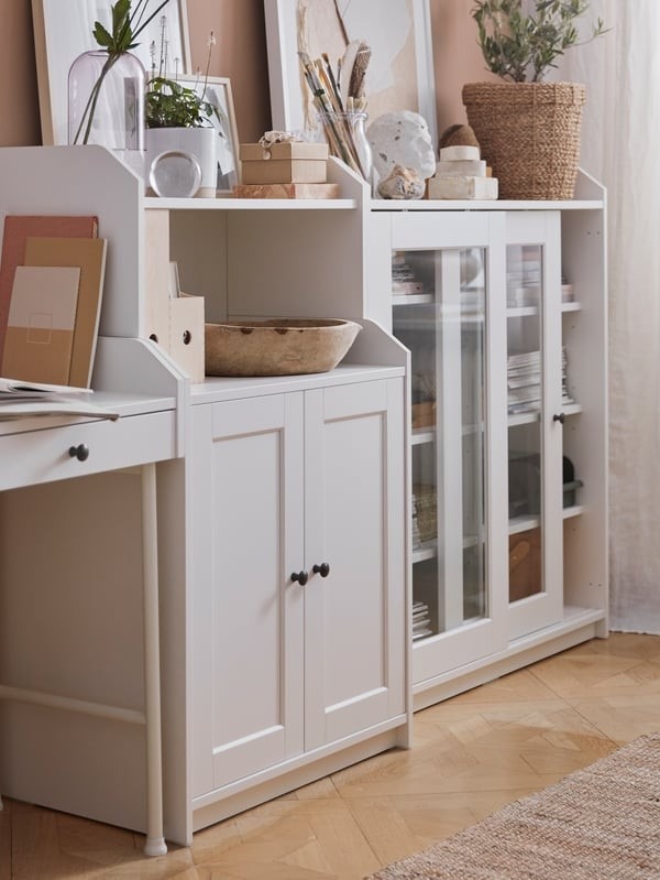 A source cabinet detail combines closed lower storage, glass-fronted display, and decorative objects above, beside the living-room desk.
