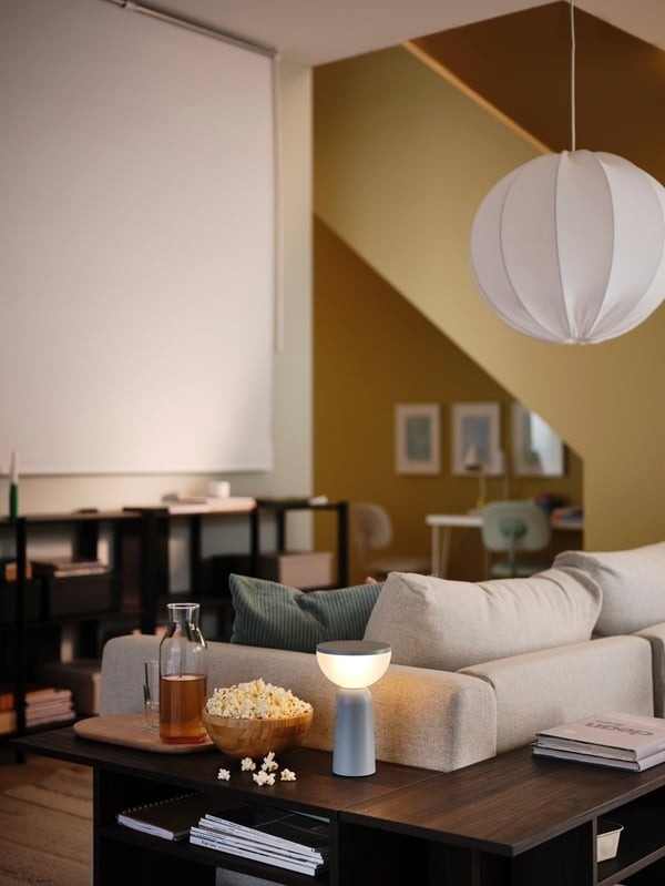 The source film-viewing setup places a lowered roller blind opposite the seating, with refreshments on the nearby surface.
