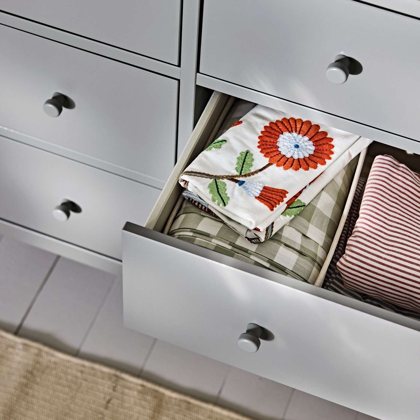 An open dresser drawer in the source contains folded patterned textiles separated by an internal box, showing the storage in use.