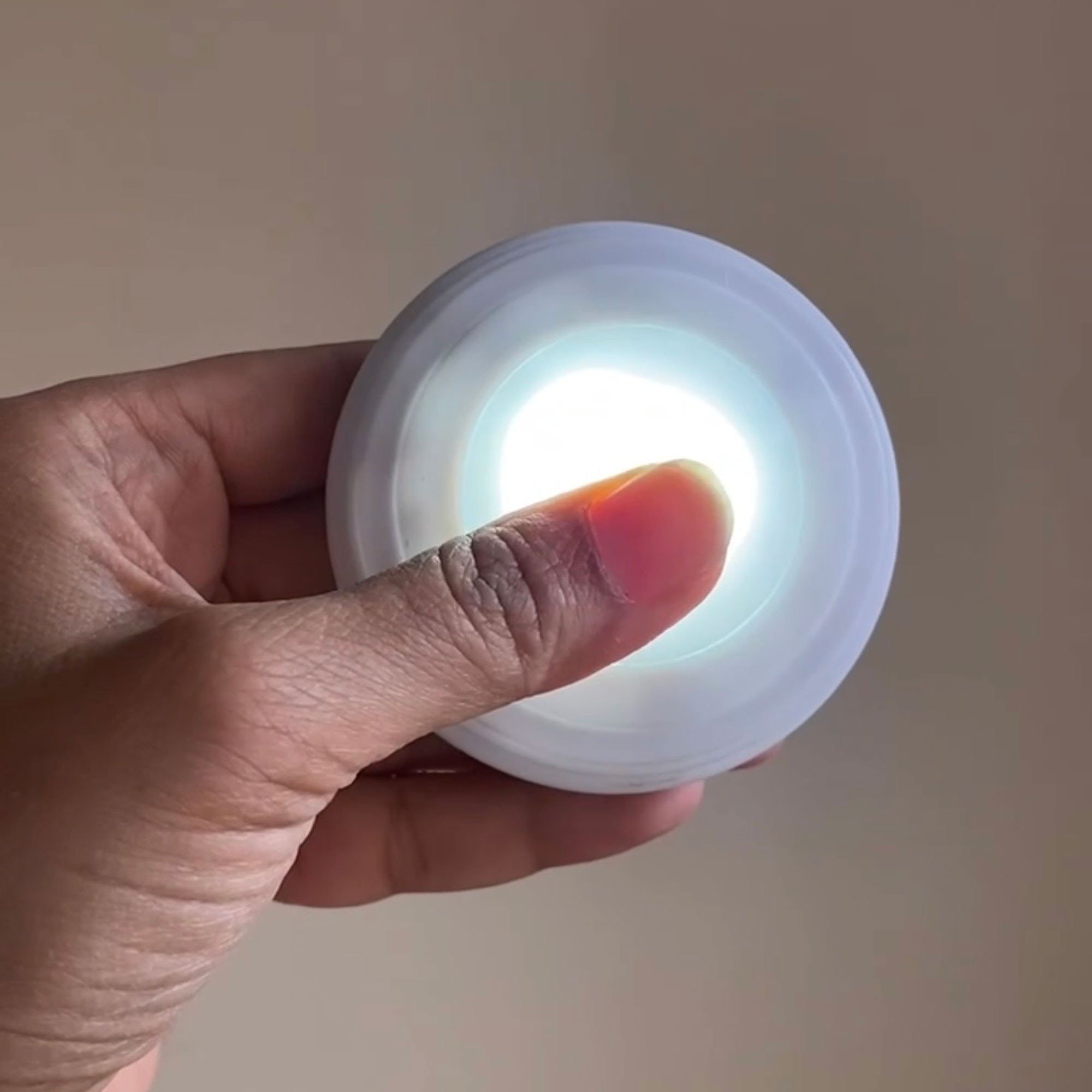 The source author holds a switched-on battery puck light, illustrating the separate light source used inside the decorative fitting.