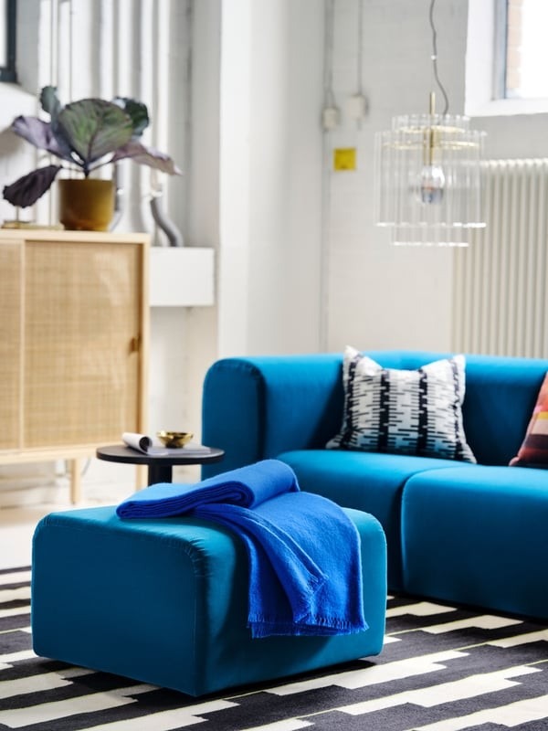 The source pairs a blue throw with a differently toned upholstered ottoman, showing coordination without an exact color match.