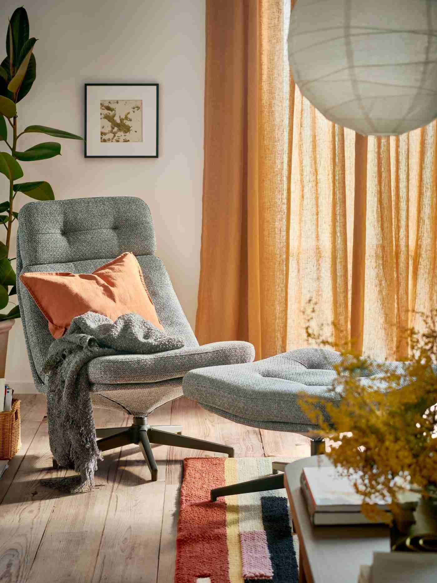 The reference places a low-profile armchair and matching footstool beside warm curtains and a paper lamp, illustrating retro silhouettes in a contemporary setting.