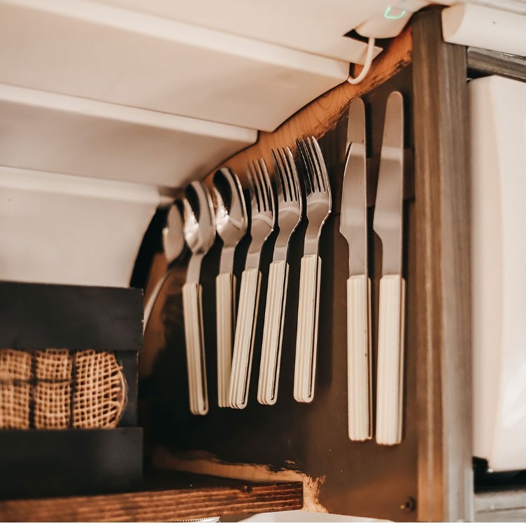 The source bus kitchen places metal cutlery on a magnetic strip, illustrating a compact storage detail rather than a complete installation specification.